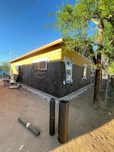 Yellow and black small house or structure under construction on wooden supports with a large tree beside it