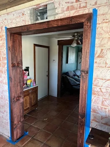 Interior doorway with wooden frame and blue protective tape, showing brick walls and brown tile floor