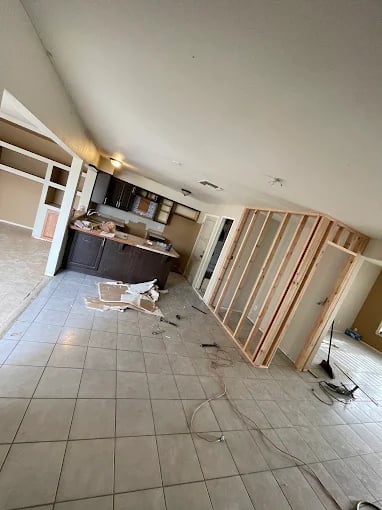 Unfinished kitchen renovation with wooden stud framing, tiled floor, and dark cabinetry visible in background