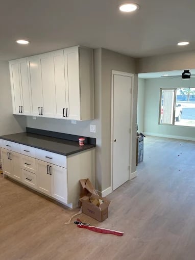 Modern kitchen with white cabinetry, dark countertop, and stainless steel appliances, with a dog lying on the wood floor in the foreground
