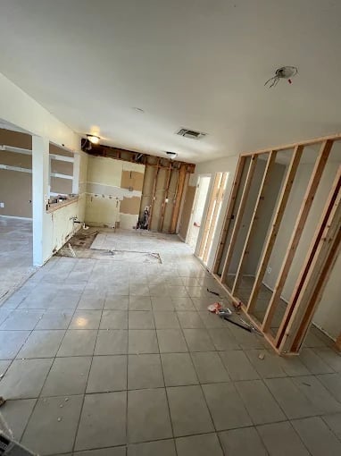 Interior of an unfinished home renovation with exposed wall framing, tile flooring, and construction materials