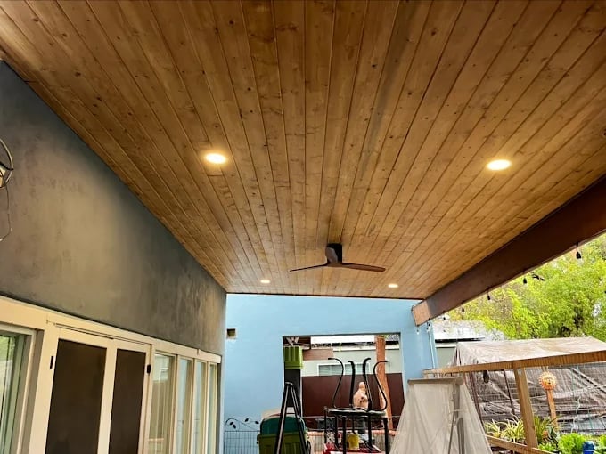 Modern patio with wooden ceiling, recessed lighting, sliding glass doors, and outdoor equipment visible in the background